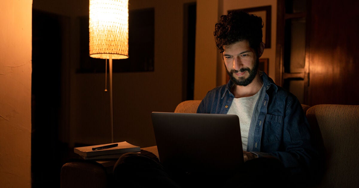 A man sitting in the dark with his laptop at home.