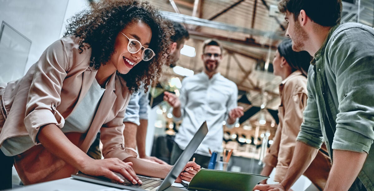 A woman standing with a laptop on a table, discussing with her friends how to become a good leader.