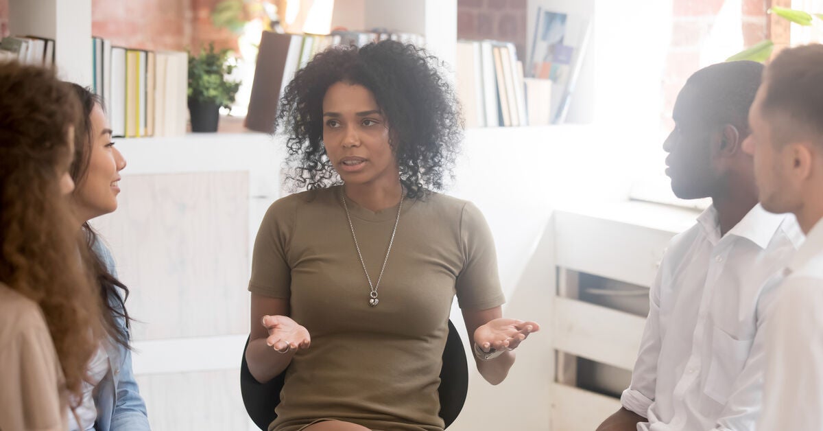 A woman leading a discussion with four other people, talking about why do people work in HR