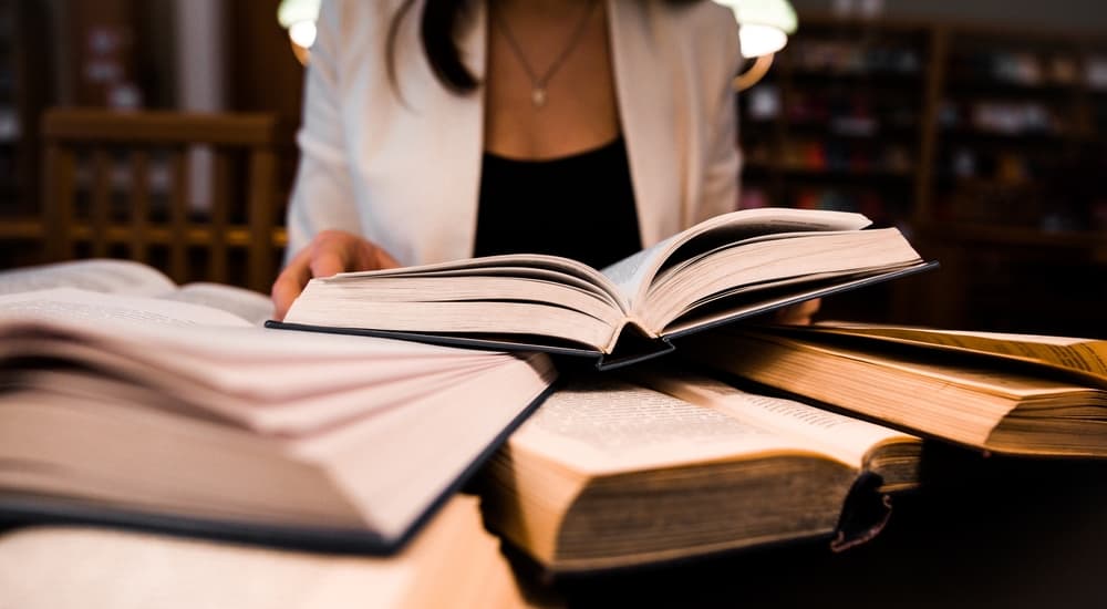 Woman studying in library with many book open on her table.