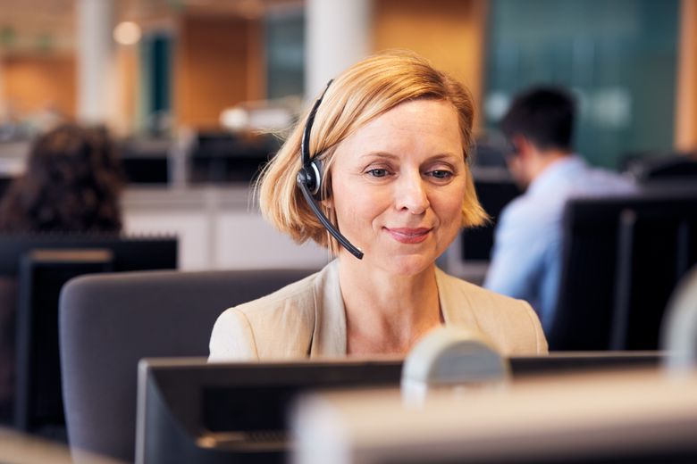 Mature Businesswoman Wearing Telephone Headset Talking To Caller In Customer Services Department