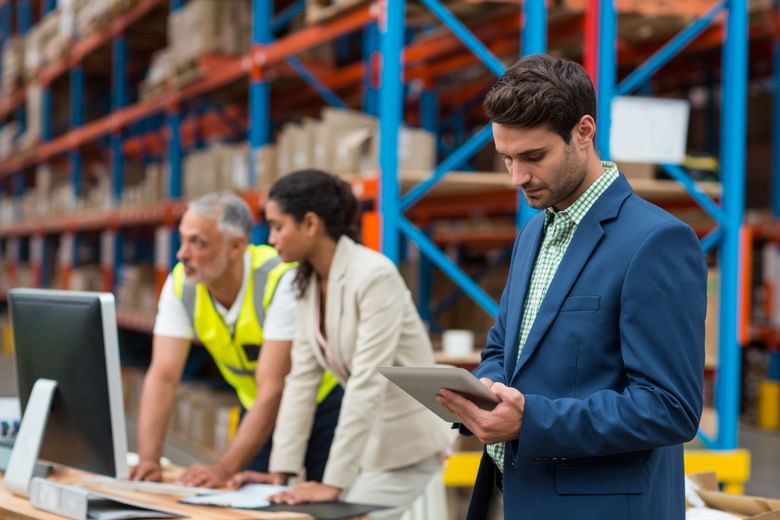 A male supply chain manager checking his notes while standing in a warehouse