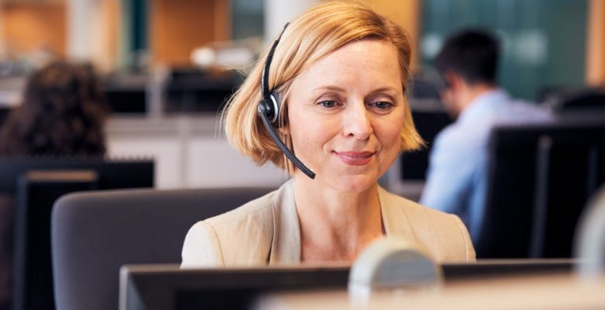 Mature Businesswoman Wearing Telephone Headset Talking To Caller In Customer Services Department