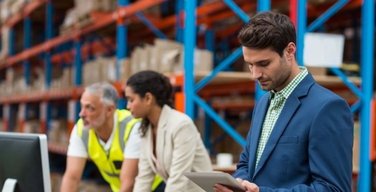 A male supply chain manager checking his notes while standing in a warehouse